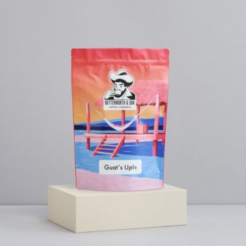 A 1 kilo bag of Guat's Up! sits atop an ivory coloured platform.